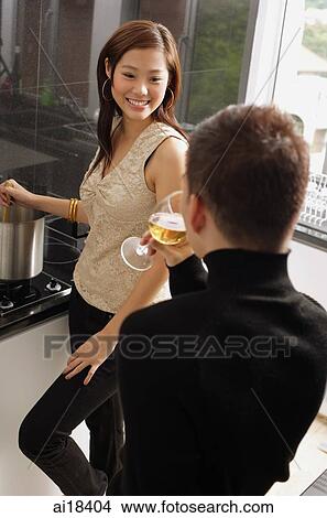 Couple in kitchen, woman cooking at stove, man drinking wine glass View Large Photo Image Picture - Couple in kitchen, woman cooking at stove, man drinking wine glass. Fotosearch