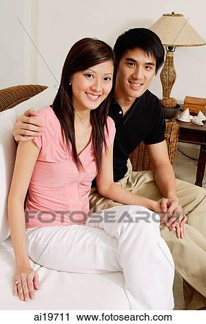 Stock Image - Couple in living room, looking at camera. Fotosearch