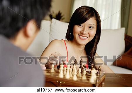 Stock Photo - Couple in living room, playing chess, woman facing camera. Fotosearch
