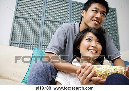 Couple in living room with bowl of popcorn, looking away View Large Photo Image Stock Photo - Couple in living room with bowl of popcorn, looking away. Fotosearch
