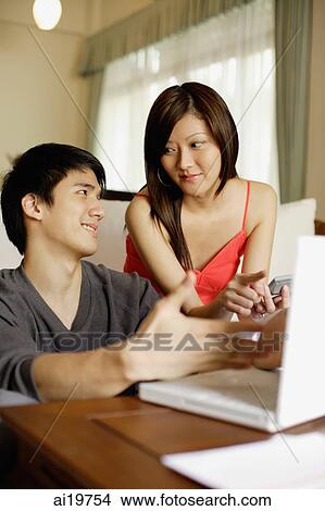 Couple in living room, with laptop and calculator, discussing expenses View Large Photo Image Picture - Couple in living room, with laptop and calculator, discussing expenses. Fotosearch