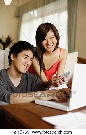 Stock Photography - Couple in living room, with laptop and calculator. Fotosearch
