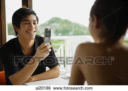 Couple in restaurant, man using mobile phone to take a picture of woman opposite from him View Large Photo Image Stock Photograph - Couple in restaurant, man using mobile phone to take a picture of woman opposite from him. Fotosearch