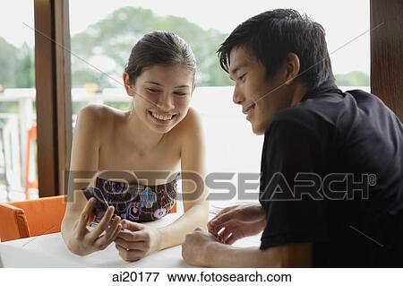 Couple in restaurant, woman showing man a mobile phone View Large Photo Image Stock Photo - Couple in restaurant, woman showing man a mobile phone. Fotosearch