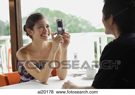 Couple in restaurant, woman using mobile phone to take a picture of man opposite from her View Large Photo Image Stock Photo - Couple in restaurant, woman using mobile phone to take a picture of man opposite from her. Fotosearch
