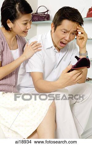 Picture - Couple in shoe shop, man holding shoe, making a face. Fotosearch