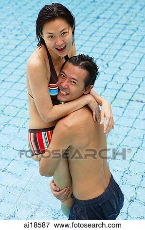 Stock Photo - Couple in swimming pool, man carrying woman, both smiling at camera. Fotosearch