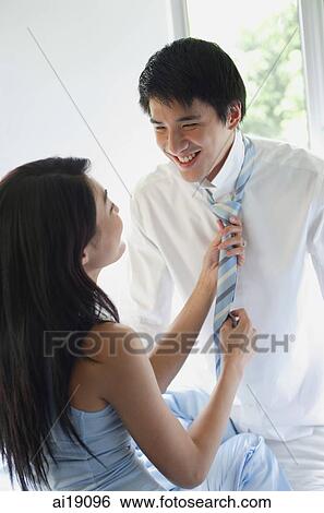 Stock Photograph - Couple looking at each other, woman pulling man's tie. Fotosearch