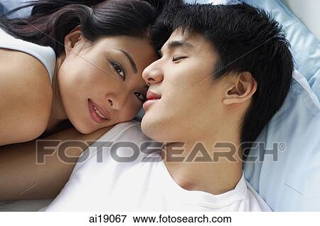 Stock Photo - Couple lying in bed, woman smiling at camera. Fotosearch