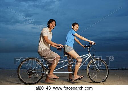 Couple on beach, sitting on tandem bicycle, smiling at camera View Large Photo Image Stock Image - Couple on beach, sitting on tandem bicycle, smiling at camera. Fotosearch