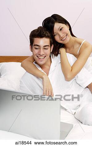 Couple on bed, looking at laptop View Large Photo Image Picture - Couple on bed, looking at laptop. Fotosearch