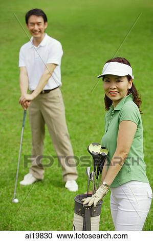 Stock Image - Couple on golf course, smiling at camera. Fotosearch