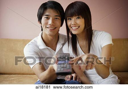 Stock Image - Couple on sofa, holding TV remote control. Fotosearch
