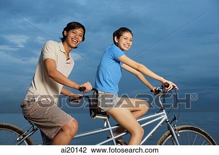 Stock Image - Couple on tandem bicycle, smiling at camera. Fotosearch