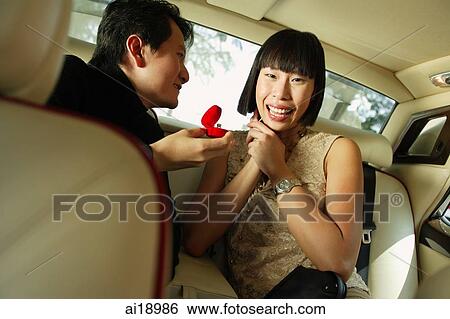 Couple sitting in backseat of car, man holding ring box, woman smiling at camera View Large Photo Image Stock Photograph - Couple sitting in backseat of car, man holding ring box, woman smiling at camera. Fotosearch