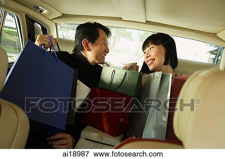 Stock Photo - Couple sitting in backseat of car, looking at each other, shopping bags on their laps. Fotosearch