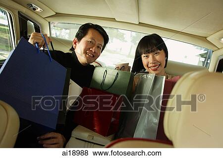 Stock Photo - Couple sitting in backseat of car, shopping bags on their laps. Fotosearch