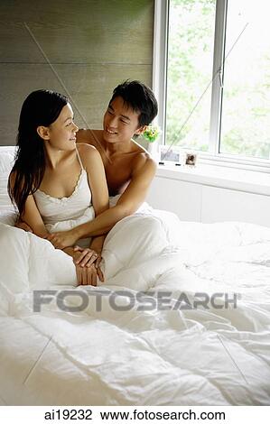 Couple sitting in bed, looking at each other View Large Photo Image Stock Image - Couple sitting in bed, looking at each other. Fotosearch