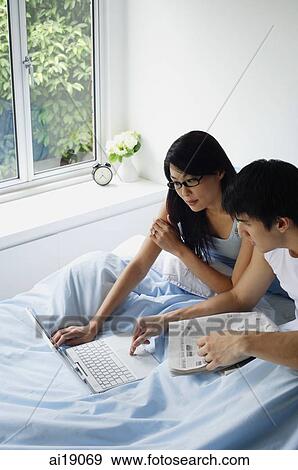 Couple sitting in bed, using laptop View Large Photo Image Stock Photo - Couple sitting in bed, using laptop. Fotosearch