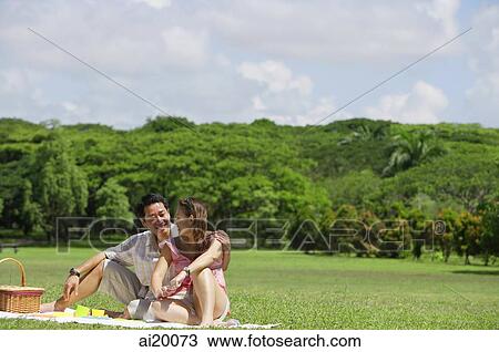 Stock Image - Couple sitting in park, having a picnic. Fotosearch