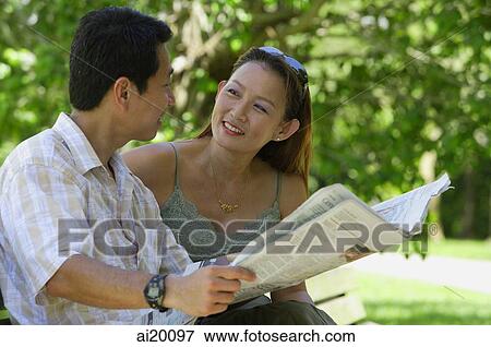 Couple sitting on bench, looking at each other, man holding newspaper View Large Photo Image Stock Photo - Couple sitting on bench, looking at each other, man holding newspaper. Fotosearch