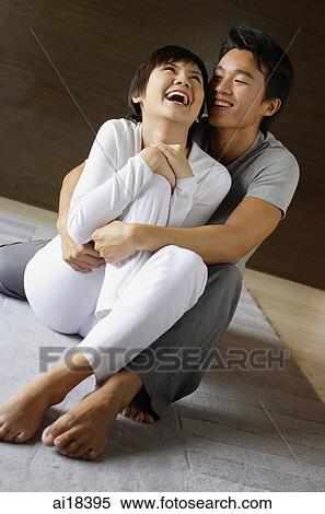 Couple sitting on floor, man embracing woman from behind, woman laughing View Large Photo Image Stock Photography - Couple sitting on floor, man embracing woman from behind, woman laughing. Fotosearch
