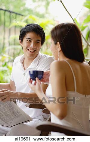Couple sitting on patio, man with newspaper, woman holding cup View Large Photo Image Stock Image - Couple sitting on patio, man with newspaper, woman holding cup. Fotosearch