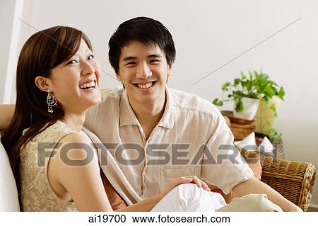 Couple sitting on sofa, smiling at camera View Large Photo Image Stock Image - Couple sitting on sofa, smiling at camera. Fotosearch