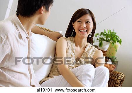 Couple sitting on sofa, woman hugging knees, smiling at man View Large Photo Image Stock Image - Couple sitting on sofa, woman hugging knees, smiling at man. Fotosearch