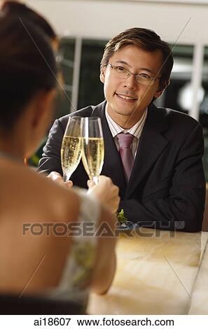 Stock Photo - Couple sitting opposite each other, toasting with champagne glasses. Fotosearch