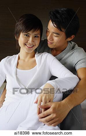 Stock Photo - Couple sitting side by side, embracing, woman smiling at camera. Fotosearch