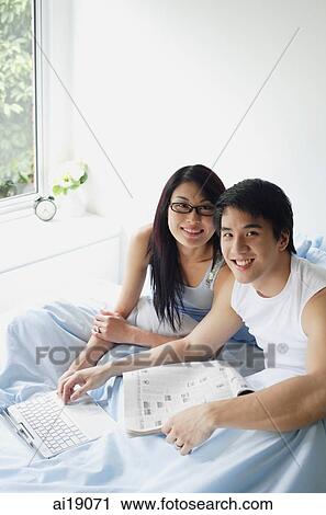 Couple sitting side by side in bedroom with laptop, smiling at camera View Large Photo Image Stock Image - Couple sitting side by side in bedroom with laptop, smiling at camera. Fotosearch