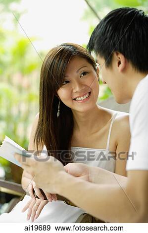 Stock Photo - Couple sitting side by side, looking at each other, man holding newspaper. Fotosearch