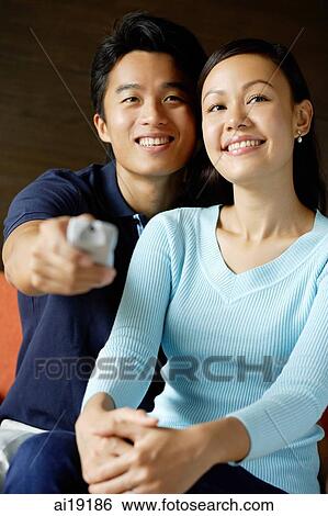 Couple sitting side by side, man holding TV remote control View Large Photo Image Stock Photograph - Couple sitting side by side, man holding TV remote control. Fotosearch