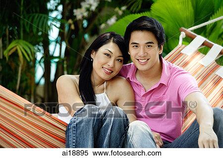 Stock Photography - Couple sitting side by side on hammock, portrait. Fotosearch