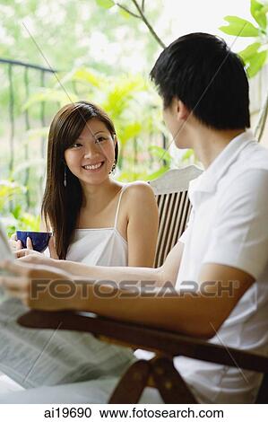 Couple sitting side by side on patio, man holding newspaper, woman holding cup View Large Photo Image Stock Image - Couple sitting side by side on patio, man holding newspaper, woman holding cup. Fotosearch