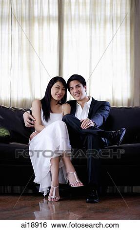 Couple sitting side by side on sofa, smiling at camera View Large Photo Image Stock Photograph - Couple sitting side by side on sofa, smiling at camera. Fotosearch