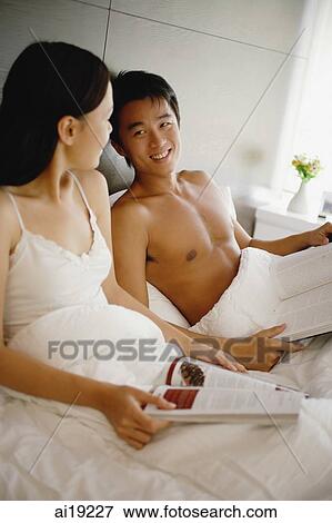 Couple sitting up in bed, holding book and magazine View Large Photo Image Stock Photo - Couple sitting up in bed, holding book and magazine. Fotosearch