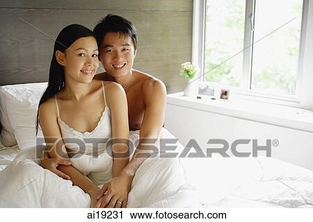 Stock Image - Couple sitting up in bed, looking at camera. Fotosearch
