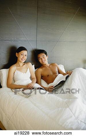 Couple sitting up in bed, with book and magazine, smiling at camera View Large Photo Image Stock Photo - Couple sitting up in bed, with book and magazine, smiling at camera. Fotosearch