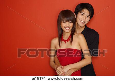 Couple standing against red wall, man hugging woman from behind View Large Photo Image Picture - Couple standing against red wall, man hugging woman from behind. Fotosearch