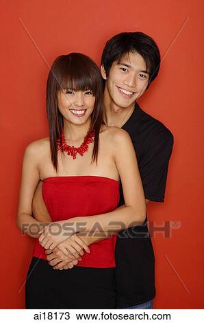 Couple standing against red wall, smiling at camera View Large Photo Image Stock Image - Couple standing against red wall, smiling at camera. Fotosearch