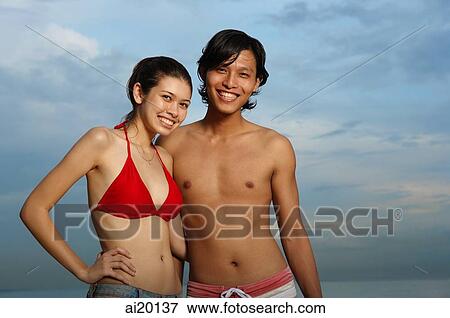 Stock Photo - Couple standing against sky at dusk, smiling. Fotosearch