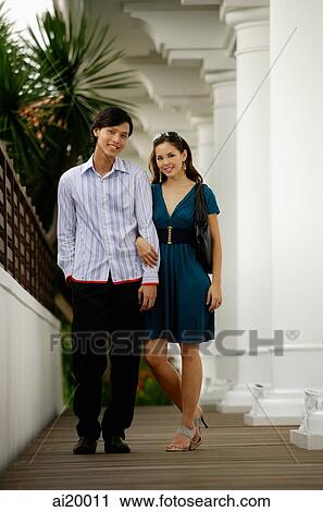 Couple standing arm in arm, looking at camera View Large Photo Image Stock Image - Couple standing arm in arm, looking at camera. Fotosearch