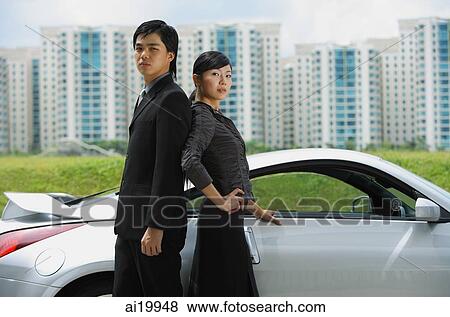 Couple standing back to back, next to sports car View Large Photo Image Stock Photo - Couple standing back to back, next to sports car. Fotosearch