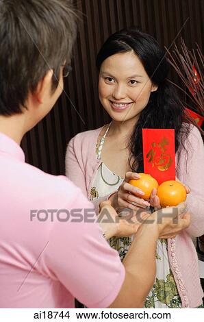 Couple standing face to face, exchanging oranges and red packet View Large Photo Image Picture - Couple standing face to face, exchanging oranges and red packet. Fotosearch