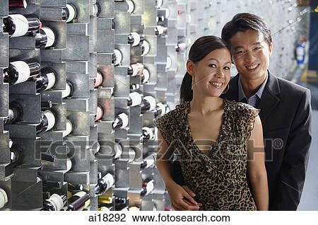 Stock Image - Couple standing in wine cellar, looking at camera. Fotosearch