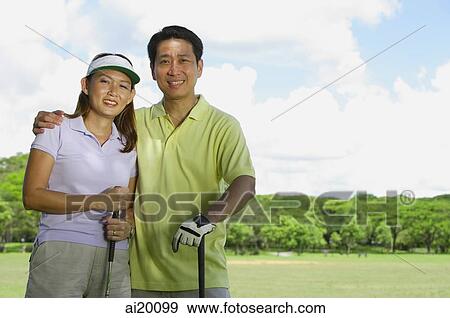 Couple standing side by side, holding golf clubs View Large Photo Image Stock Photo - Couple standing side by side, holding golf clubs. Fotosearch