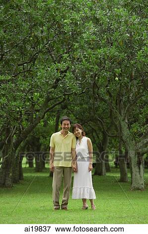 Couple standing side by side in park, looking at camera View Large Photo Image Stock Photo - Couple standing side by side in park, looking at camera. Fotosearch