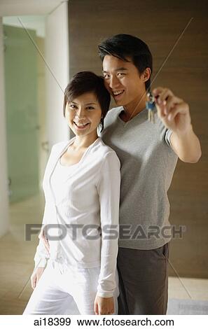 Couple standing side by side looking at camera, man holding key View Large Photo Image Stock Photo - Couple standing side by side looking at camera, man holding key. Fotosearch